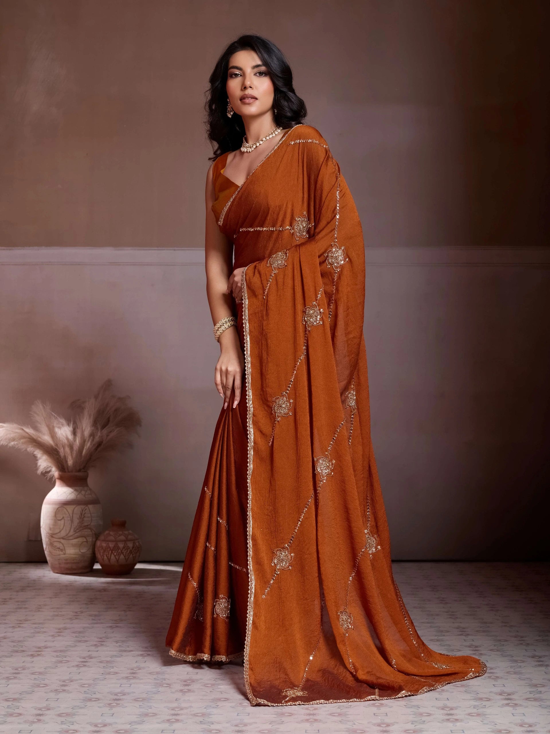 Woman in a rust-colored saree with gold patterns standing against a neutral background